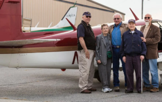 Group of smiling adults standing in front of plane.