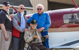 Smiling group of men posed in front of a small plane.