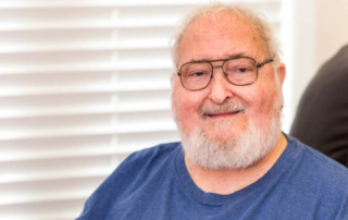Masonic Village resident Harry Meyers, a smiling seated man with white hair and glasses.