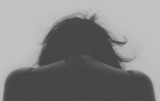 Black and white image of woman with depression with her head down.