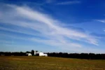 Farmhouse on large, open field with blue sky behind it.