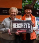 Two senior women smiling while holding huge Hershey's chocolate bar.