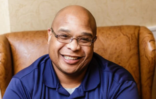 Justin Thomas, a smiling man with glasses, seated indoors.