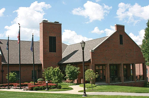 Large brick building with trees and nicely kept lawn in front of it.