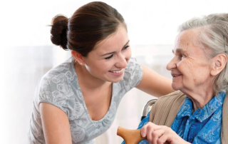 Smiling woman leaning down to talk to seated senior woman.