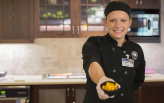Young woman holding out chopped fruit in a small dish.