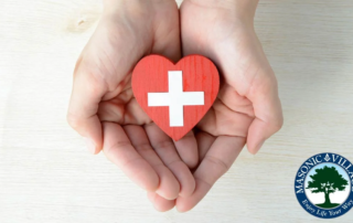 Hands holding wooden heart with a white First Aid sign.