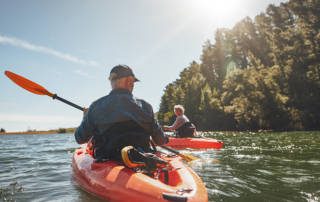 Outdoor shot of mature man canoeing in the lake with woman in background. Couple kayaking in the lake on a sunny day.