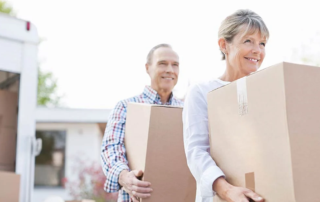 Senior couple carrying moving boxes outdoors.