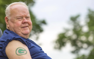 Bill Riggle, a smiling senior man showing off a Green Bay packers tattoo.