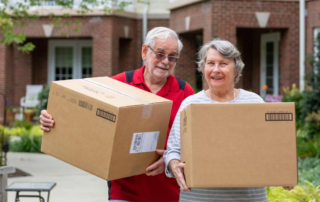 Smiling senior couple carrying moving boxes outdoors.