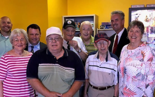 Group of adults smiling together indoors at a check presentation.