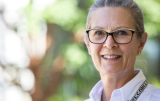 Valerie Gray, a smiling woman with glasses standing outdoors.