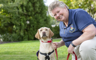 Jo-Anne Karnes, a smiling woman with short hair, kneeling down next to a service dog