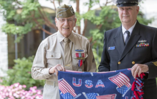 Hospice volunteers Herb Ridyard and Larry Wolford dressed in military uniforms and holding an American flag blanket.