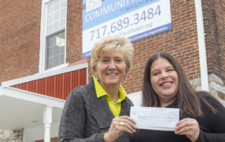 Two smiling women holding up check for Community Cupboard