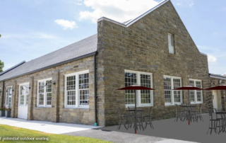 A large stone cafe building with rendering of picnic tables in front of it.