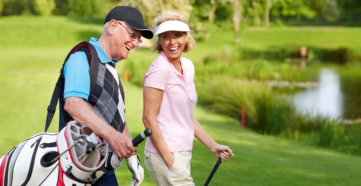 Couple laughing as they carry golfing equipment.