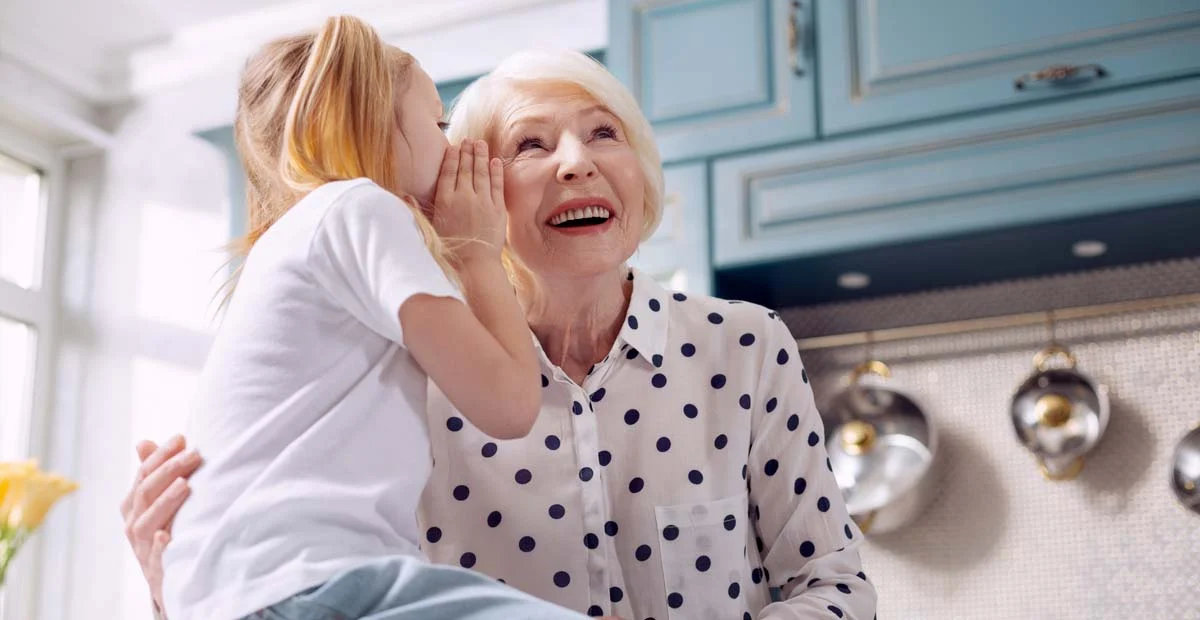 Little girl whispering to her grandmother in kitchen.