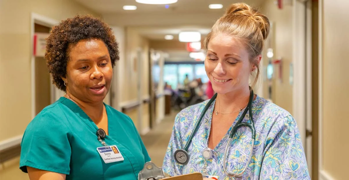 Two nurses smiling while looking at a chart together.