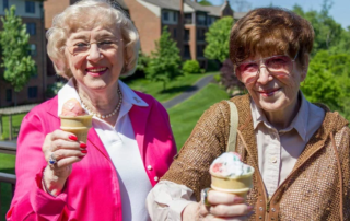 Senior women holding out ice cream cones while smiling.