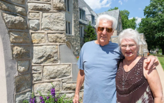 Don and Pat Gibble, a smiling couple standing in front of large stone apartment building.