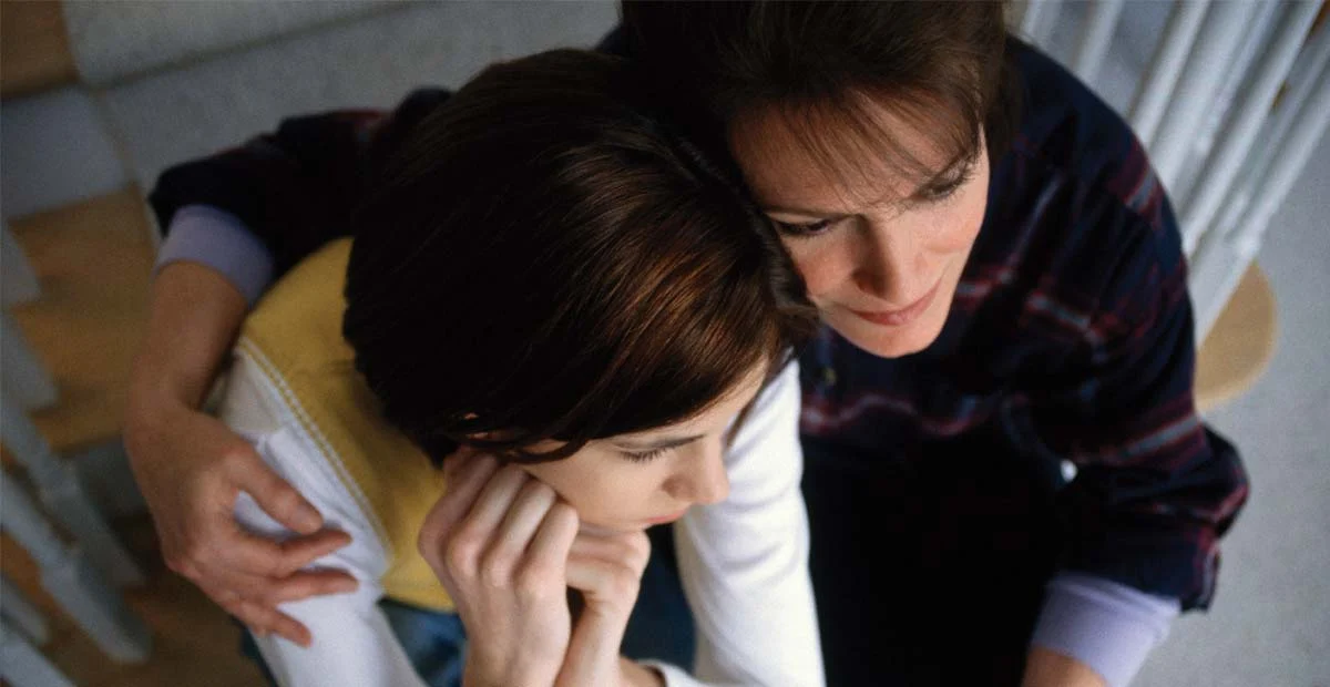 Adult woman hugging child while sitting together.