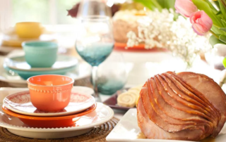 Easter Ham on a table set with flowers and colorful cups and saucers.
