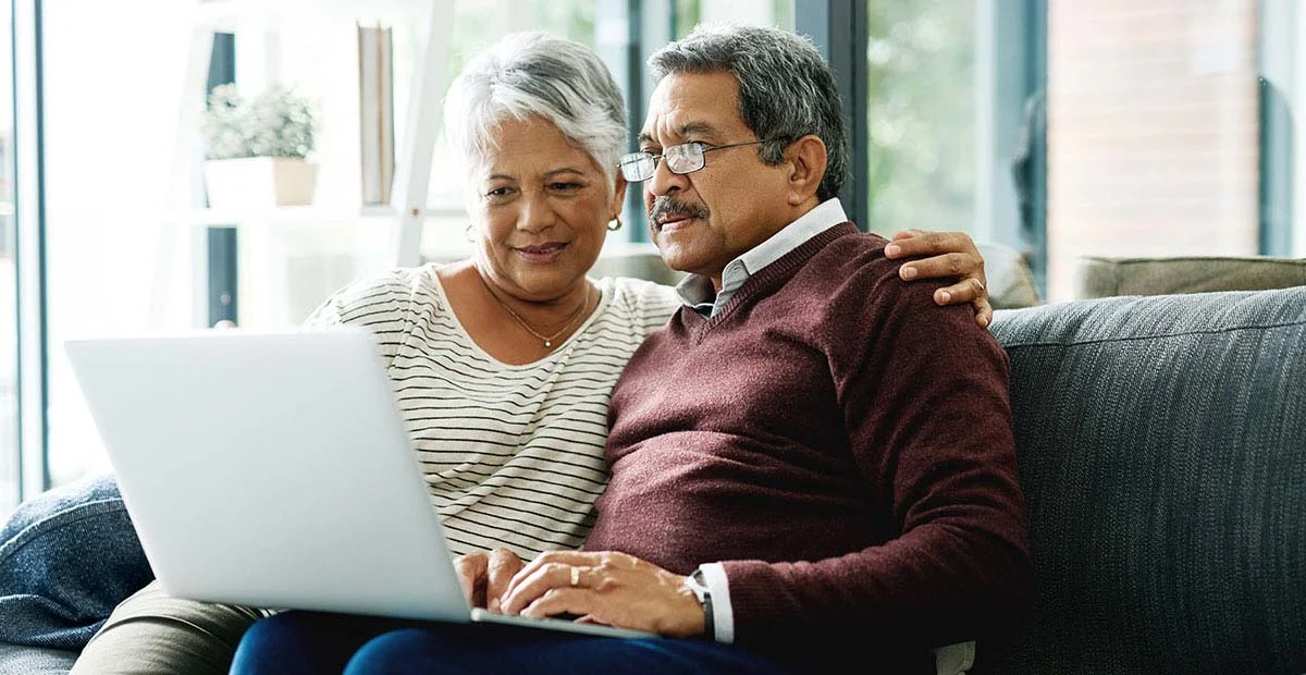 Senior couple seated on couch with laptop.