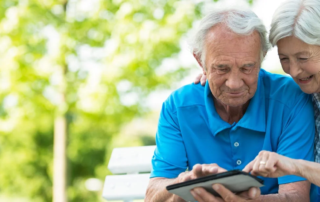 Older couple with tablet sitting outdoors.