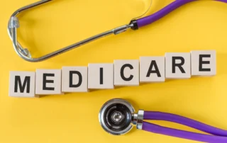 Medicare word written on cube shape wooden blocks on yellow table with stethoscope