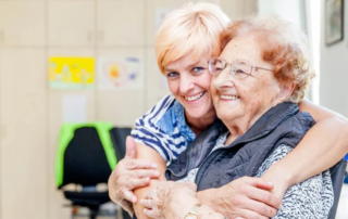 Woman hugging elderly woman in wheelchair.
