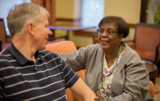 Smiling senior man talking with nurse while both are seated.