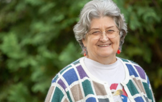 Smiling senior woman with glasses standing outdoors.