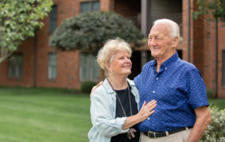 Smiling senior couple standing together outdoors in front of brick building.