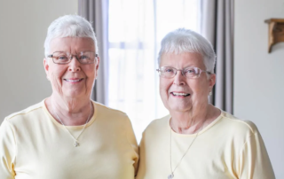 Portrait of Kitty and Lois, sisters who are dressed alike and both smiling.