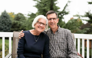 Portrait of the Evankos, a smiling couple on their porch.