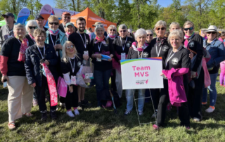 Smiling group preparing for Breast Cancer walk behind Team MVS sign.