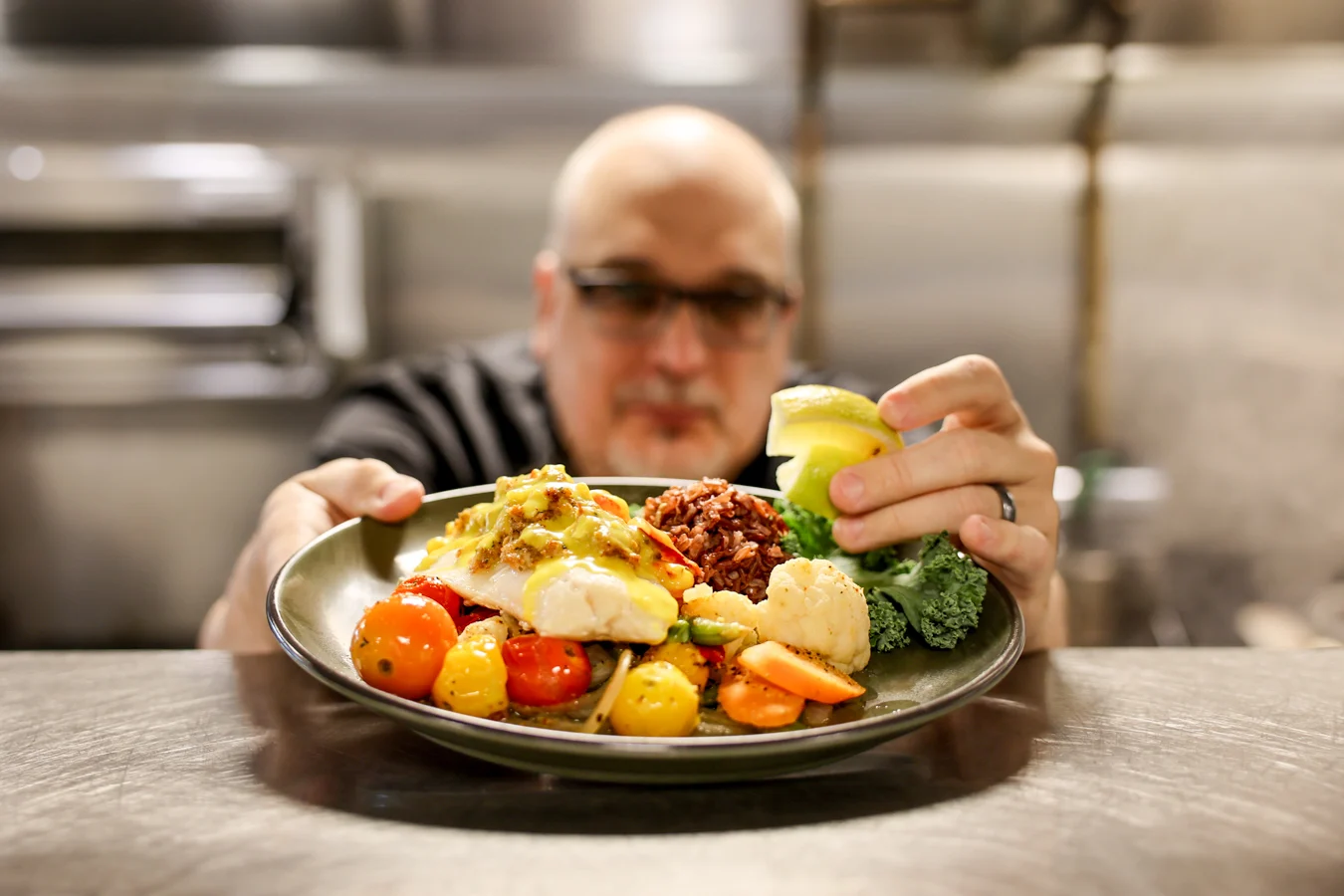 Closeup of chef holding out colorful plate of food, man is out of focus