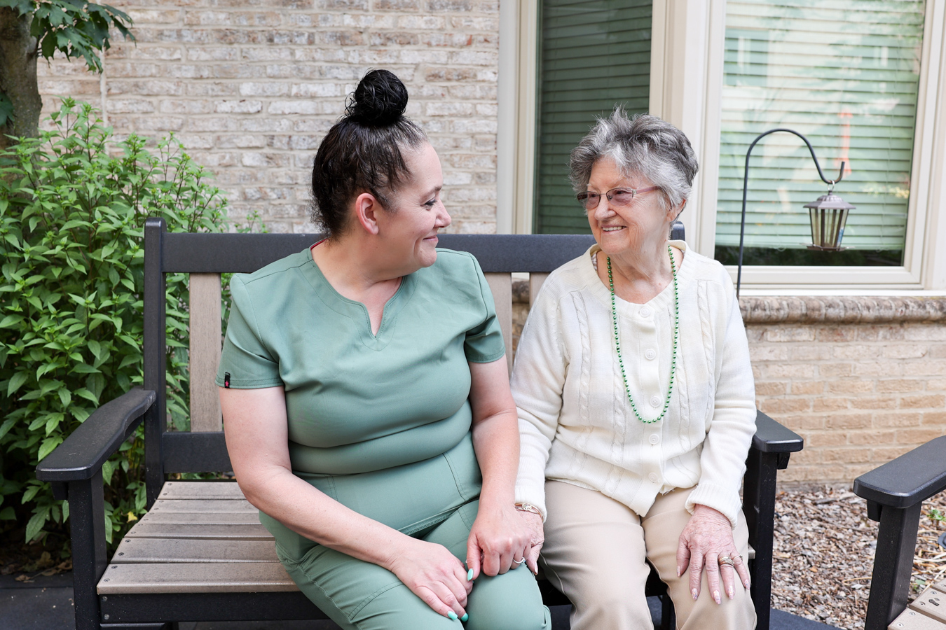 Resident sitting outdoors and holding hands with aide