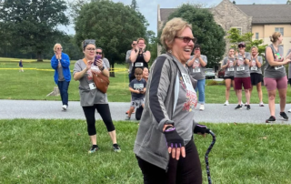 Maureen Jackson, a smiling woman walking with a cane during the Harvest Hustle while a crowd behind her applauds.