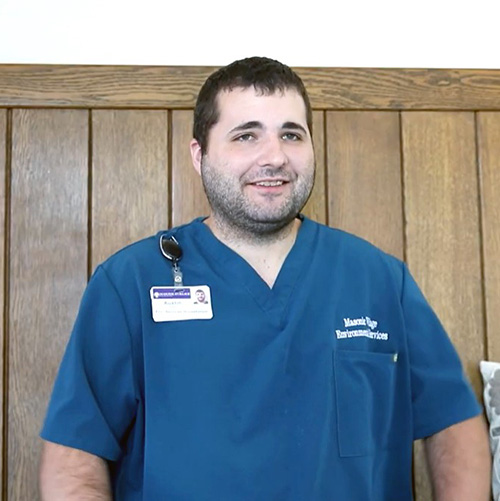 Smiling man with short, dark hair in blue scrubs.