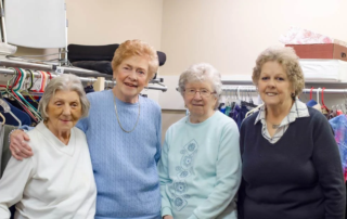 Pennywise Volunteers, a smiling group of senior women standing in front of clothing racks.