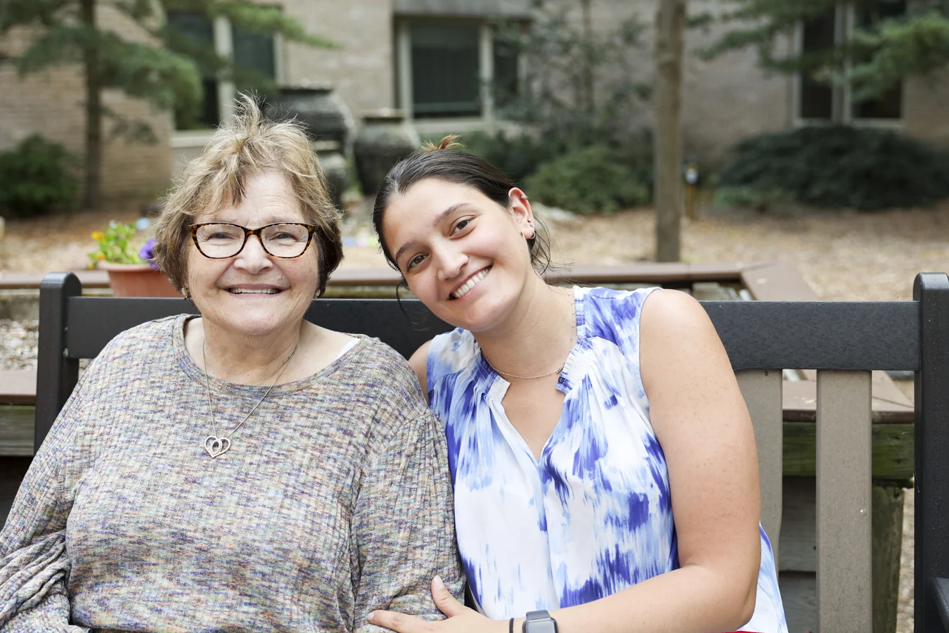 Two seated women, one mature, seated on a bench outdoors together.