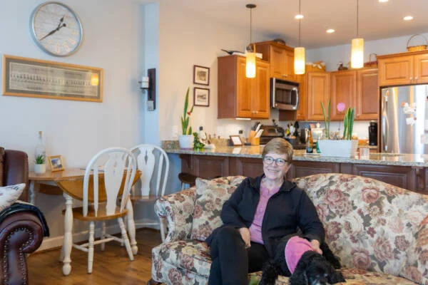 Smiling senior woman and her dog seated on a couch inside her apartment.