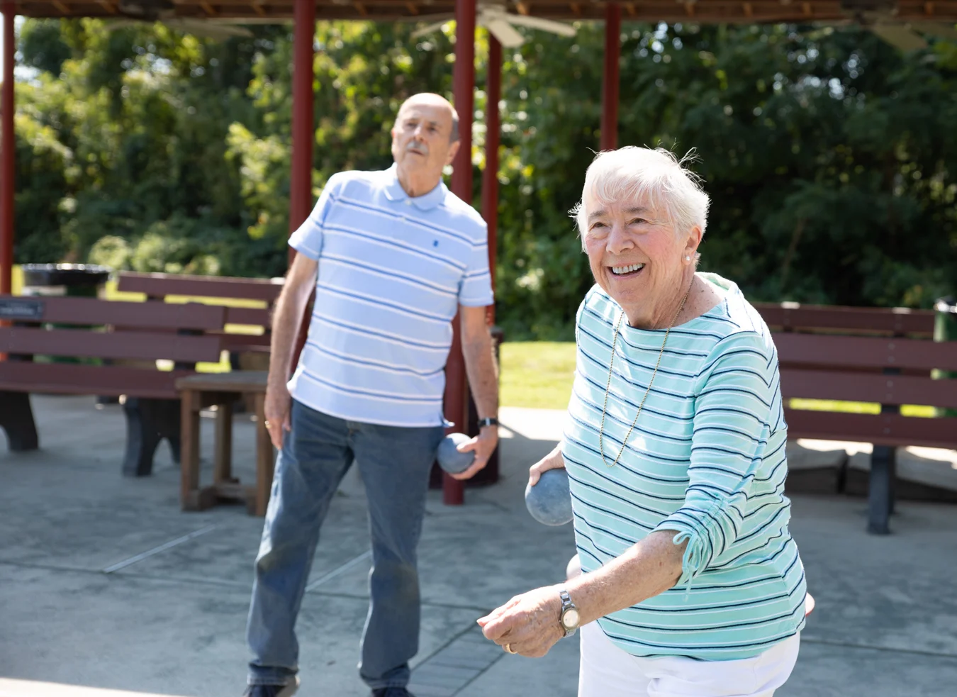 Smiling senior woman and man playing bocce outdoors.