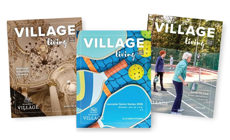 Overlapping issues of Village Living magazine, the covers feature an ornate room interior, pickleball equipment, and women playing pickleball on a court outdoors.