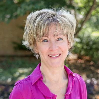 1W8A0393 Smiling woman with short hair standing outdoors.