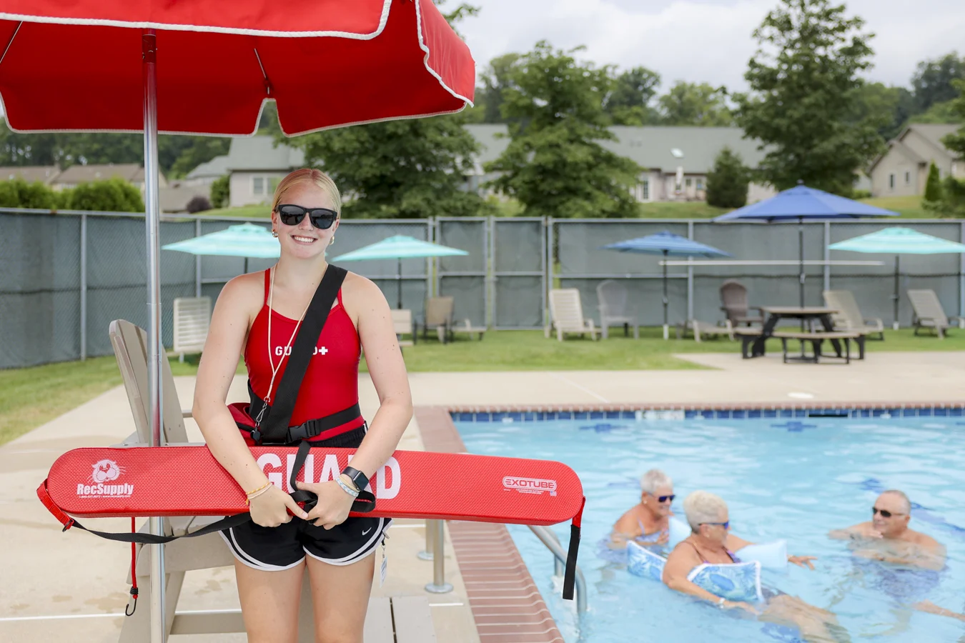 Smiling lifeguard standing in front of a chair beside a pool.