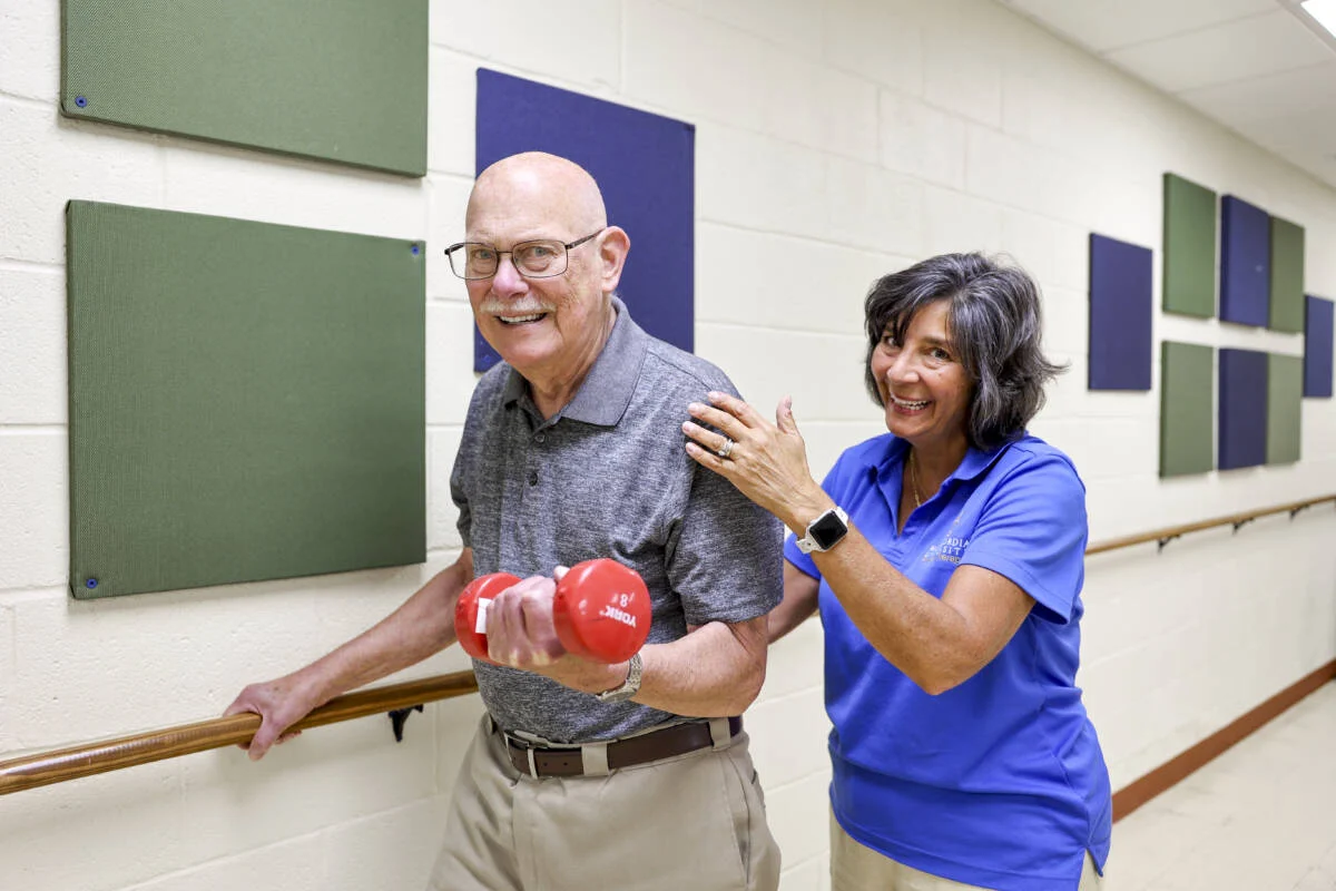Smiling senior man lifting a weight while working with a physical therapist.